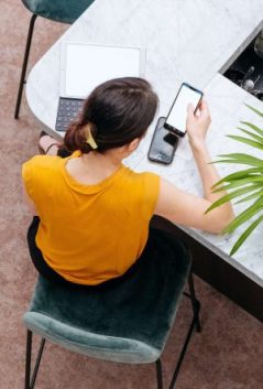 Young woman checking credit repair service prices on her mobile phone at a desk.